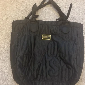 Svart väska från Marc Jacobs - Snygg svart väska från Marc Jacobs med ett stort innerfack och dragkedja. Man får plats med hur mycket som helst och den är helt perfekt för att bära med sig allt man behöver.