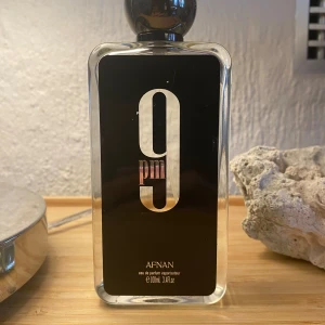 Afnan 9PM Eau de Parfum - Säljer en elegant parfymflaska från Afnan med namnet 9PM. Flaskan är genomskinlig med en svart etikett och stor vit text. Den rymmer 100 ml av doften men 90ml kvar. Perfekt för kvällsanvändning.