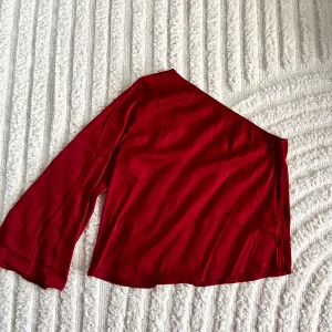 Röd oneshoulder topp från Rut&Circle - Snygg röd oneshoulder topp från Rut&Circle. Perfekt för en kväll ute eller en speciell tillställning. Den har en elegant design med en lång ärm och är tillverkad i ett mjukt material.