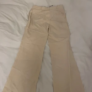 Beige kostymbyxor - Snygga beige kostymbyxor med en klassisk design. Ser lite ut som linnebyxa. Byxorna har en rak passform med lite bootcut och är perfekta för en stilren look. De har fickor både fram och bak samt hällor för bälte.