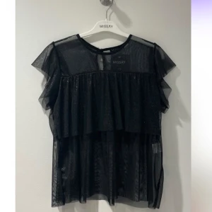 Svart topp från Missay - Snygg svart transparent topp från Missay med volangdetaljer. Kortärmad design som ger en luftig och elegant look. Passar perfekt till fest! Toppen är helt ny med prislapp kvar! Säljer den pga att det är försent att returnera den. Nypriset är 329kr