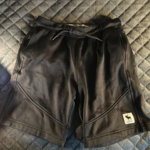 Svarta shorts från Abercrombie Kids - Snygga svarta shorts från Abercrombie Kids med elastisk midja och dragsko. Perfekta för en avslappnad stil. Har samt fickor