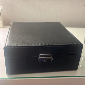 Svart smyckeskrin med spegel - Svart smyckeskrin med flera fack och en liten spegel. Perfekt att organisera ringar, armband och halsband. Insidan är klädd i mjukt material för att skydda dina smycken. Man kan även lyfta på första lagret och så är det en större yta med fickor under:) (pris kan diskuteras)