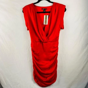 Röd omlottklänning från Mango - Snygg röd omlottklänning frånmango med draperad design och djup v-ringning. Perfekt för en kväll ute eller en speciell tillställning. Klänningen har en smickrande passform och är ärmlös.