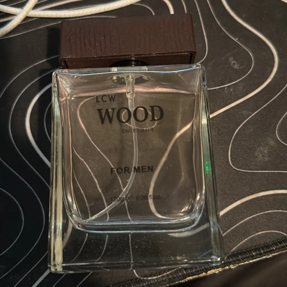 En elegant flaska med LCW Wood Eau de Toilette för män. Flaskan är genomskinlig med en stilren design och har en mörkbrun kork som ger en naturlig känsla. Perfekt för den som gillar träiga dofter.. Perfume.