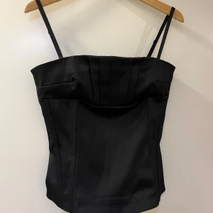 Svart korsett med dragkedja - Snygg svart korsett med justerbara axelband och dragkedja i ryggen. Perfekt för en stilren look.