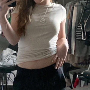 Beige kortärmad topp - Säljer en stilren beige topp med korta ärmar och djup urringning. Perfekt för en avslappnad look.