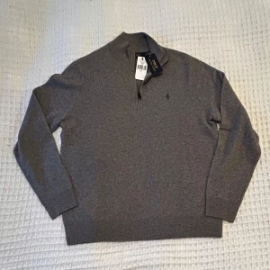 Grå tröja från Polo Ralph Lauren - Snygg grå ull tröja från Polo Ralph Lauren. Säljer då jag köpte i en för stor storlek. Helt ny bara provad en gång men aldrig använd. Lappar finns kvar fast i tröjan. Nypris 2795kr