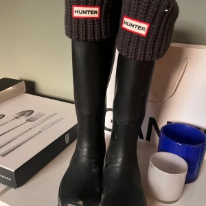 Svarta stövlar från Hunter - Säljer ett par klassiska svarta stövlar från Hunter med stickade innestrumpor till för extra värme. Perfekta för regniga dagar och håller fötterna torra. Stövlarna har en justerbar rem med spänne på sidan för bättre passform. Sjukt snygga men för små för mig! (smutsen på bilden tvättas bort innan försäljning) 