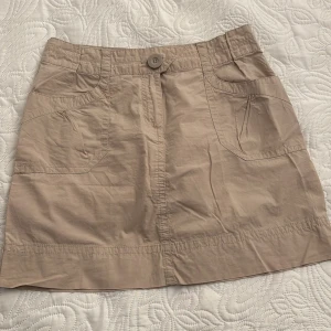 Beige kjol från H&M - Säljer en beige kortkjol från H&M i bomull. Kjolen har fickor fram och bak samt en knappdetalj i midjan. 