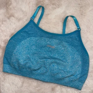 Blå linnetopp från Gymshark - Säljer en blå sporttop från Gymshark med justerbara axelband. Perfekt för träning med sin bekväma passform och stilrena design. Gymshark-loggan syns tydligt på baksidan. 