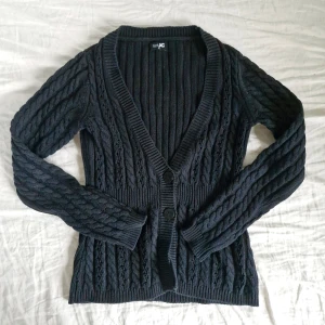 Svart stickad kofta från JC - Säljer en snygg svart stickad kofta från JC med kabelstickat mönster. Koftan har en djup v-ringning och knäpps med två stora knappar framtill. Storlek XS men passar även S. 55% bomull. Pris är diskuterbart! :)