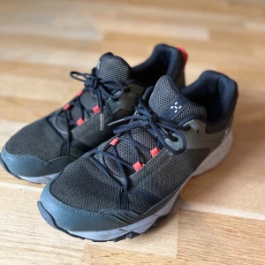 Friluftsskor från Haglöfs - Snygga och robusta sneakers från Haglöfs i svart och grått med oranga detaljer. Skorna har en slitstark sula och snörning för optimal passform. Perfekta för utomhusaktiviteter. Små i storleken, skulle säga att det är stl.43