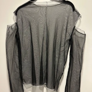 Svart mesh topp - Säljer en svart mesh topp med långärmad design och offshoulder-stil. Perfekt för en trendig look med transparent material som ger en edgy känsla.