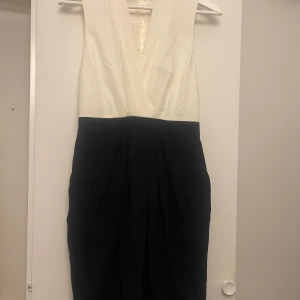 Klänning  - Elegant klänning från hm med vit överdel och svart kjol. Den har en djup v-ringning och är ärmlös. 