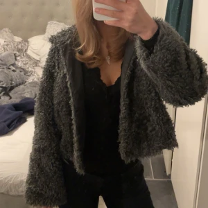 Grå teddyjacka - Mysig grå teddyjacka med croppad passform. Perfekt för att hålla sig varm och stilren under kyliga dagar. Jackan har långa ärmar och en mjuk, fluffig yta.