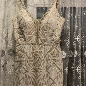 Glittrig klänning med pärlor - Säljer en fantastisk glittrig klänning med djup v-ringning och pärldetaljer. Klänningen har ett geometriskt mönster och är ärmlös med en elegant passform. Den har även en push up bh där brösten ska vara men det märks inte av! Köpt utomlands (kosovo) i en känd butik för festklänningar. Dragkedja bakom klänningen son man stänger, knappt använd! Köpt för 1000