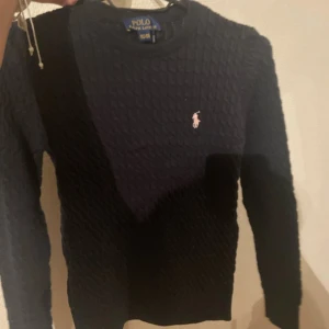 Svart stickad tröja från Ralph Lauren - Säljer en stilren svart stickad tröja från Ralph Lauren med det klassiska broderade logotypen på bröstet. Tröjan har en rund halsringning och är perfekt för kyligare dagar. Passar både till jeans och chinos för en avslappnad look. 💗✨