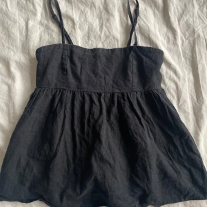 Svart linne med smala axelband - Säljer ett svart linne med smala axelband och rynkad detalj på baksidan. Perfekt för varma sommardagar. Enkel och stilren design som passar till det mesta.