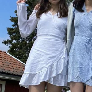 Vit omlottklänning - Säljer en söt vit omlottklänning med volangdetaljer. Klänningen har långa ärmar och en knytning i midjan. 