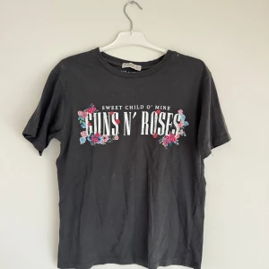 Svart Guns N' Roses t-shirt från Stradivarius - Cool svart t-shirt från Stradivarius med Guns N' Roses-tryck och texten 'Sweet Child O' Mine'. Blommiga detaljer runt texten ger en extra touch. Perfekt för rockälskare!
