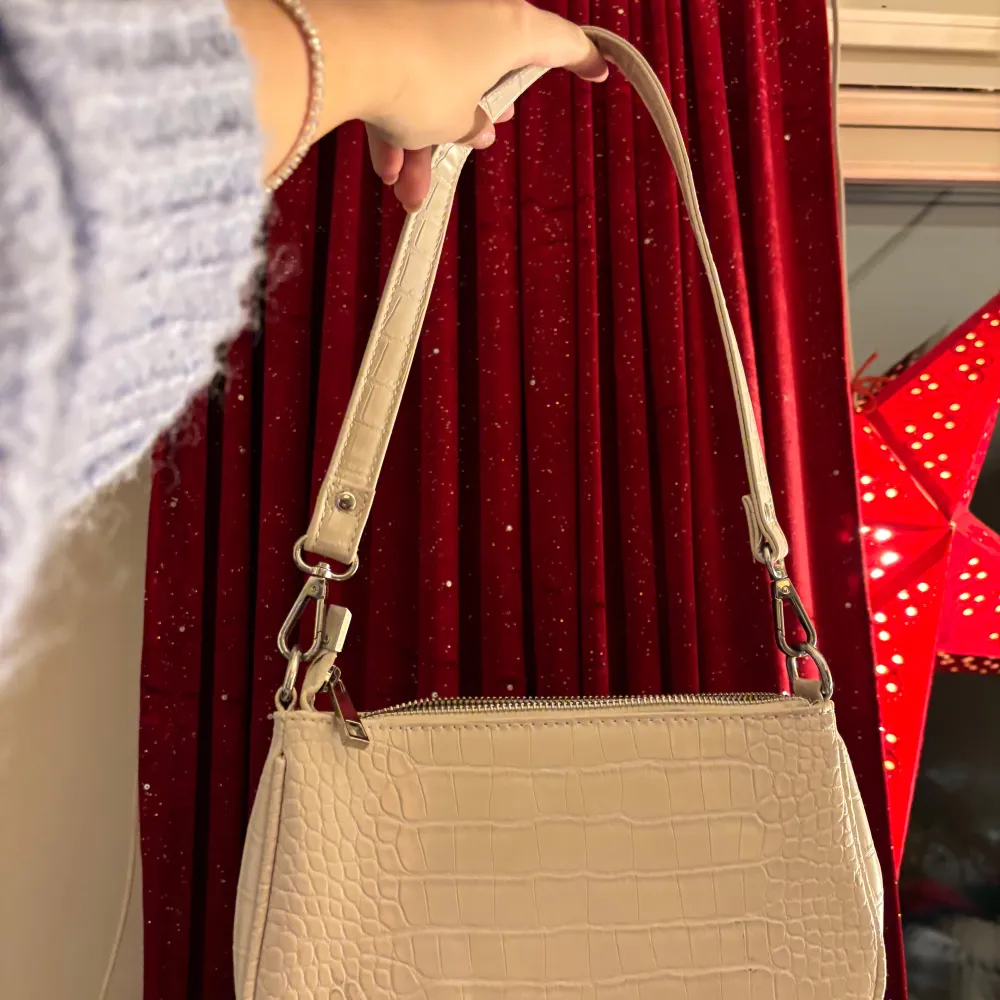 Snygg beige/cremevit axelväska från Gina Tricot med krokodilpräglat mönster. Väskan har en kortare axelrem och dragkedja upptill, samt innerfack med dragkedja. Perfekt för att bära dina dagliga nödvändigheter med stil. Inga defekter, ren och fin, mycket bra skick. Tveka inte vid frågor eller prisförslag, är öppen för mindra justeringar!. Laukut & Käsilaukut.