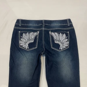 Lågmidjade bootcut jeans med vingar på fickorna🤩 - Midja 42 cm plus mycket stretch rakt över, gren 21 cm o innerben 74 cm💕jae 169 o xs-s o håller in mycket i midja rumpa o lår. Storlek 12 alltså L-stor M