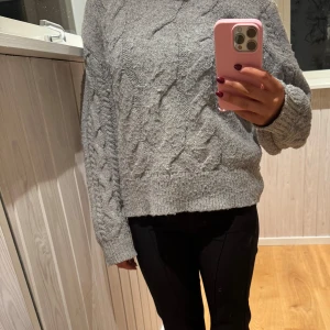 Grå stickad tröja från Gina Tricot - Mysig grå stickad tröja från Gina Tricot med kabelstickat mönster. Tröjan har ribbade kanter vid ärmslut och nederkant. Där är lite nopprig💗