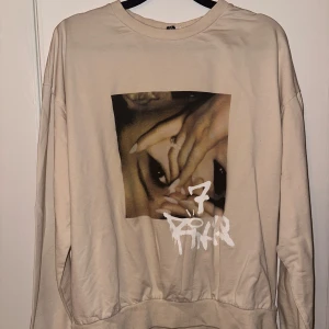 Beige sweatshirt med Ariana Grande tryck - Säljer en beige sweatshirt med ett unikt tryck på framsidan. Tröjan har långa ärmar och en avslappnad passform. Perfekt för en casual look.