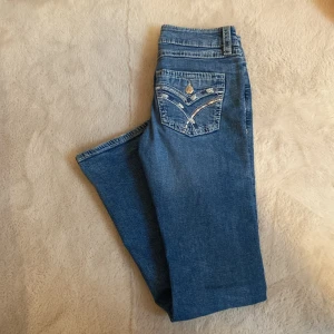 Blå jeans från Gina Tricot - Snygga blå jeans från Gina Tricot med dekorativa bakfickor. Perfekta för en avslappnad stil. Klassisk design med knapp och dragkedja framtill.