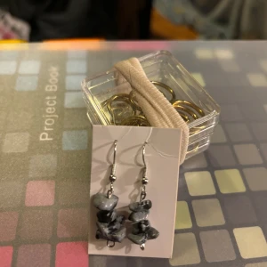 Gråsvarta örhängen med stenar - Snygga örhängen med gråsvarta stenar i en unik form. Perfekta för att ge en stilfull touch till din outfit. De hänger på en silverfärgad krok.