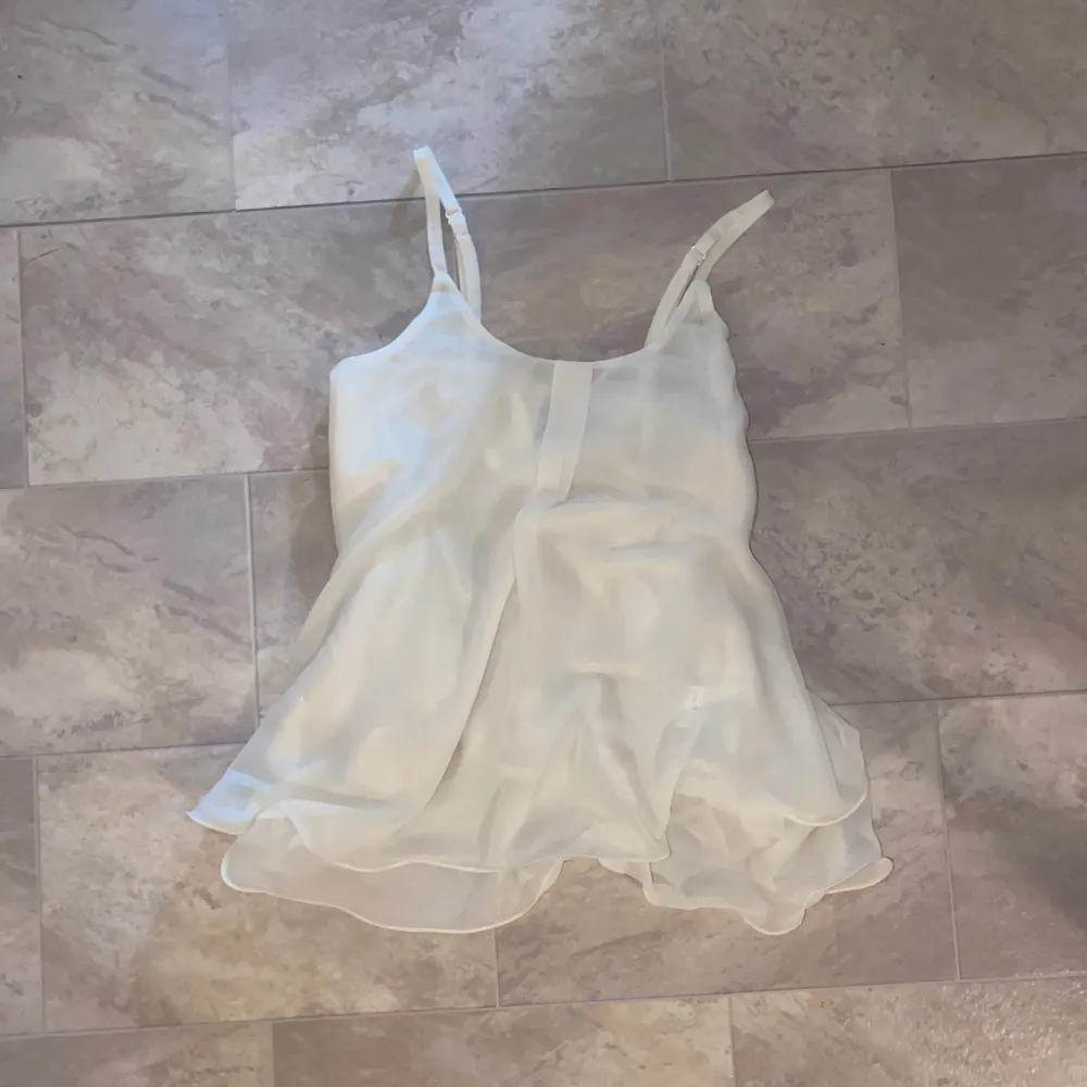 Säljer en luftig och elegant vit ärmlös topp med tunna axelband. Perfekt för varma dagar eller som ett lager under en kavaj. Toppen har en lätt och fladdrig design som ger en feminin touch. (Aldrig använd). Yläosat.