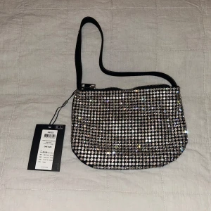 Silverfärgad axelväska från Pieces - Snygg och glittrig axelväska från Pieces i silverfärg. Väskan är täckt med glittrande paljetter och har en enkel axelrem. Perfekt för att lägga till lite bling till din outfit.