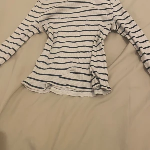 Vit och svart randig topp från Divided - Säljer en stilren vit och svart randig topp från Divided. Toppen är ribbad med långa ärmar och har en bekväm passform. Perfekt för en avslappnad look.