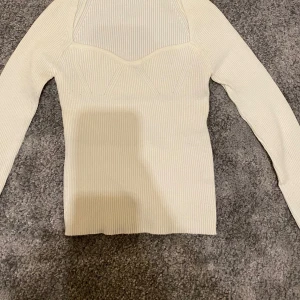 Vit ribbad topp - Snygg vit ribbad topp med långärmad design och unik struktur vid bysten. Perfekt för en stilren look. Storlek Xs