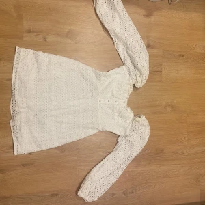 Vit klänning(student) - En kort vit klänning med broderie anglaise som har långa ärmar. materialet är bomull och i storlek 38 euro. klänningen är väldigt bekväm och jag har använt den en gång för min studenter 2024. klänningen är i bra kvalitet och har inga skador eller smuts alls.