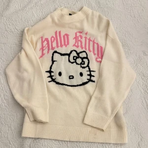 Vit Hello Kitty tröja från H&M - Säljer en söt vit tröja från H&M med Hello Kitty i svart och rosa. Tröjan har långa ärmar och ribbade kanter vid hals, ärmslut och nederkant. Perfekt för alla Hello Kitty-fans! 🐱💖
