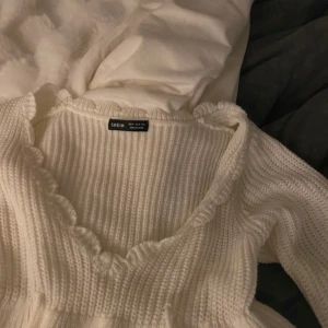 Vit ribbad tröja från SHEIN - Säljer en stilren vit ribbad tröja från SHEIN. Tröjan har en v-ringad design med volangdetaljer längs halsringningen. Perfekt för en mysig och trendig look.
