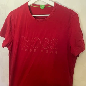 Röd t-shirt från Hugo Boss - Snygg röd t-shirt från Hugo Boss med tryckt logotyp på framsidan. Den har en klassisk rund hals och korta ärmar. Perfekt för en stilren och avslappnad look.