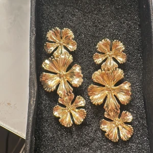 Guldiga blommiga örhängen - Rostfrittstål, Snygga guldiga örhängen i form av blommor. De har en glittrig yta som fångar ljuset fint. Perfekta för att ge en extra touch till din outfit.