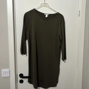 Olivgrön klänning från HM - Snygg olivgrön klänning från HM i en enkel och stilren design. Klänningen har trekvartsärmar och en rund halsringning, perfekt för en avslappnad look. Tillverkad i ett mjukt och bekvämt material.