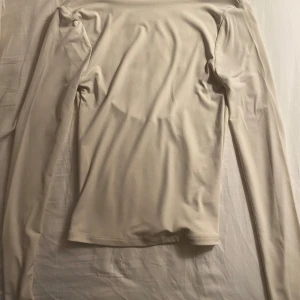 Beige långärmad topp med öppen rygg - Säljer en stilren beige långärmad topp med en djup öppen rygg. Perfekt för en elegant och modern look. Toppen är i ett mjukt och stretchigt material som ger en bekväm passform.