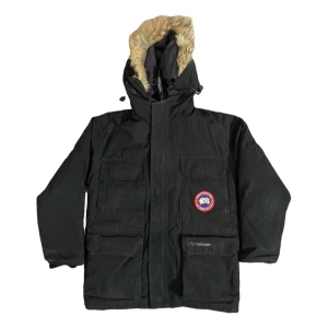 Svart dunjacka från Canada Goose - Säljer en svart dunjacka från Canada Goose med pälsfodrad huva då den är för liten, personen i bilden är ca 170cm lång. pris kan diskuteras vid snabbaffär