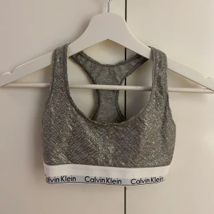 Calvin Klein Top/bh - Topp från Calvin Klein med glittrigt mönster och elastiskt band med logga. Bandet 29 cm, men blir större i och med stretch. Strl S men skulle säga mer XS. Köpt på Macy’s i USA, inte använd mycket 