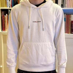 Saint Laurent hoodie  - Säljer en smygg vit hoodie från Saint Laurent. Den är i ett mycket bra skick. Nypris ligger på runt 4999kr och här kan de köpas för bara 1999k. Vid fler frågor är det bara att skriva.
