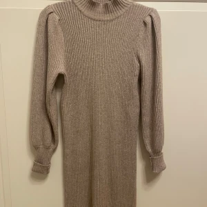 Beige stickad klänning från ONLY - Snygg beige stickad klänning från ONLY i storlek S. Klänningen har långa ärmar och en ribbad design som ger en stilren look. Perfekt för kyligare dagar med sin mysiga och varma känsla. Lite trasigt i en söm.