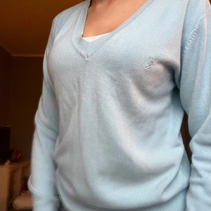 Ljusblå tröja - Säljer en stilren ljusblå tröja från Gina Tricot med v-ringning. Tröjan har långa ärmar och en diskret logga på bröstet. 
