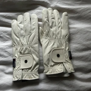Vita handskar från CWD - Snygga vita handskar från CWD med justerbar rem och knappdetalj. Perfekta för ridning med bra grepp och stilren design. Storlek 11 enligt etiketten.Alsrig använda.Skulle säga att dom är väldigt väldigt stora därför jag säljer dom. Köpta på Falsterbo horse show 🫶🏻☺️