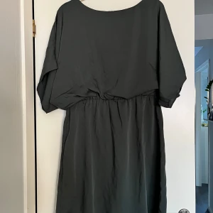 Mörk grå/grön klänning från Bubbleroom Moa Mattsson  - Elegant mörkgrå/grön klänning från Bubbleroom med en lös passform och kortärmad design. Klänningen har en rund halsringning och en diskret dragkedja i ryggen för enkel påklädning. Perfekt för en stilren look.
