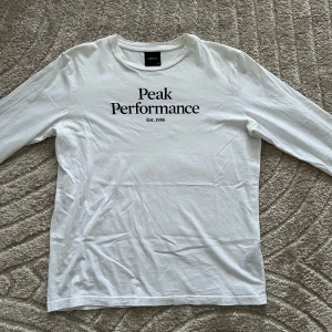 Vit långärmad tröja från Peak Performance - Säljer en stilren vit långärmad tröja från Peak Performance med tryck på bröstet. Perfekt för en avslappnad look. Tröjan är i storlek S och har en klassisk passform.